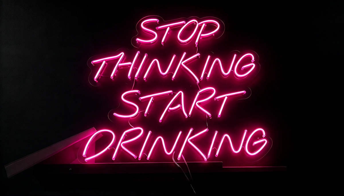 Pink neon sign reading “Stop Thinking Start Drinking” on a dark background.
