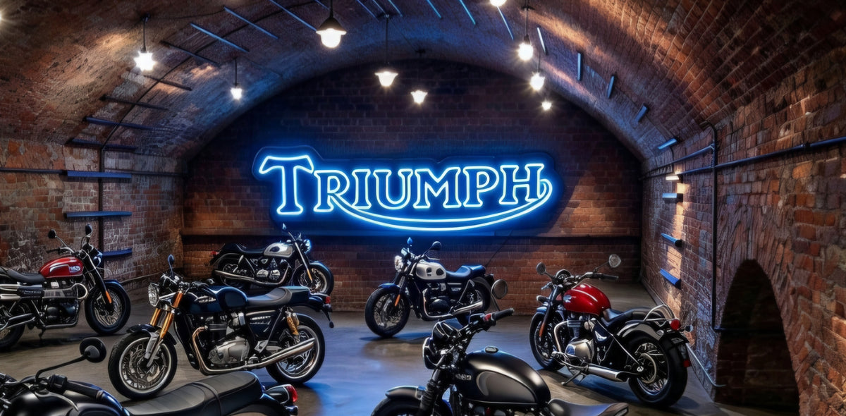 Classic Triumph motorcycles displayed in a brick arched garage, with a glowing blue Triumph sign on the wall.