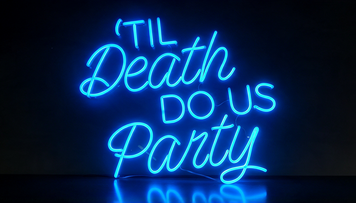 Blue neon sign reading “’Til Death Do Us Party,” in mixed cursive and block lettering on a dark background.
